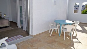 Eine Terrasse mit einem runden Tisch und vier Stühlen, eine Tür zu einem anderen Raum und ein Blick auf ein Gebäude im Hintergrund.