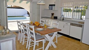 Eine moderne Küche mit weißen Schränken, einem Holzespeise-tisch und Blick auf einen Swimmingpool.