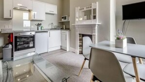 Une cuisine moderne avec des meubles blancs, un four encastré et un four à micro-ondes. On y trouve une table à manger avec des chaises et une petite plante en pot.