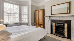 Une chambre à coucher avec un lit, une armoire en bois, une cheminée et une grande fenêtre.