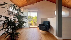 A spacious room with wooden flooring, a large potted plant, a chair, and a view through a sliding glass door. - House between pond and ocean - ideal for a family (Lège-Cap-Ferret)