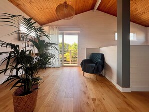 A spacious room with wooden flooring, a large potted plant, a chair, and a view through a sliding glass door. - House between pond and ocean - ideal for a family (Lège-Cap-Ferret)