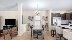 A modern kitchen with a dining area, featuring a long table, chairs, a chandelier, and artwork on the walls. - Modern Comfort Spacious Home 5BR 3BA (Greensboro)