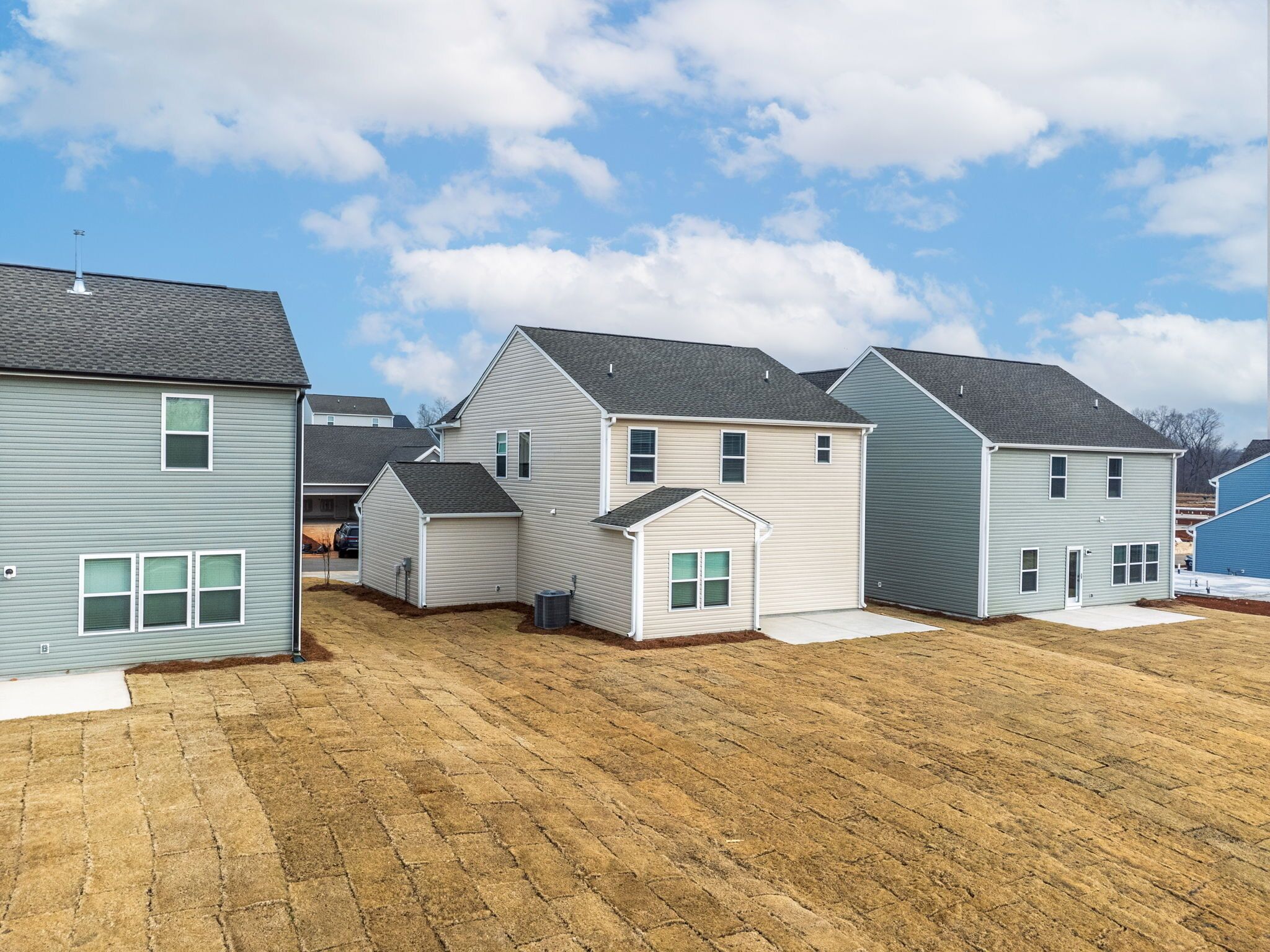 A row of single-story houses with attached garages, a paved driveway, and a clear sky.