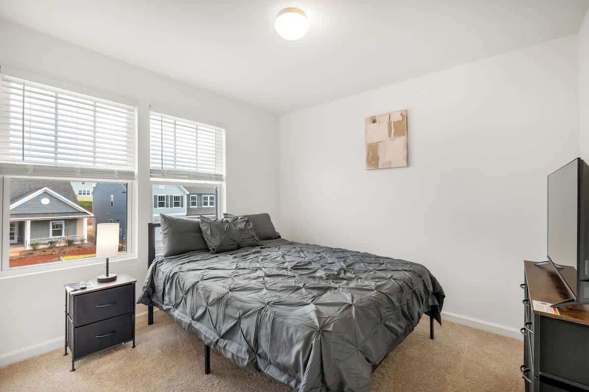 A bedroom with a bed, a nightstand, a TV, and a window with blinds.