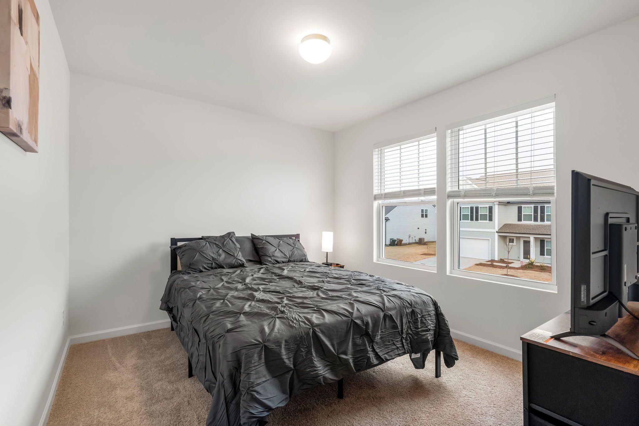 Ein Schlafzimmer mit Bett, Fernseher und Fenster mit Jalousien.
