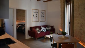 A cozy living room with a red sofa, a wooden dining table, and two framed botanical prints on the wall. - Apartment & Boutique Meraki 2 rooms. (Ontinyent)