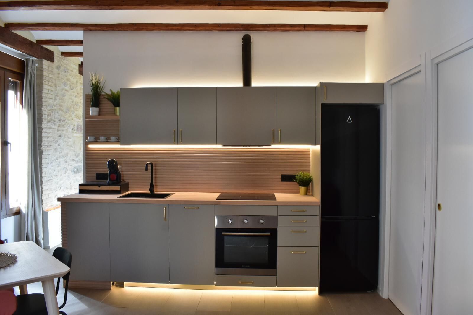 A modern kitchen with grey cabinets, a black refrigerator, and a built-in oven.