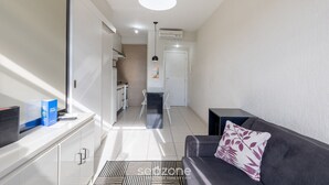 A modern living room with a sofa, a coffee table, and a TV. There is a kitchen area in the background with a dining table and chairs. - Apt w/ 1 Suite in BSB - Nrm0205 (Brasília)