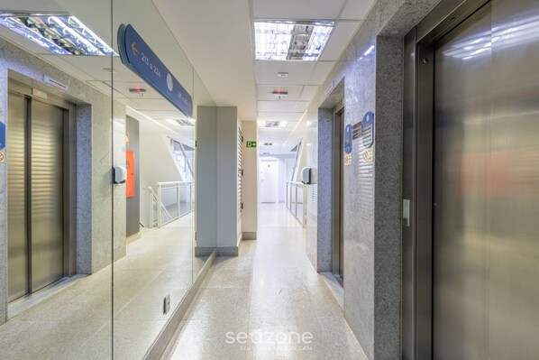 A modern hotel corridor with glass doors, a sign indicating room 213, and an elevator. - Apt w/ 1 Suite in BSB - Nrm0205 (Brasília)