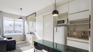 A compact hotel room with a kitchenette, a glass dining table, a black sofa, and a view of the cityscape. - Apt w/ 1 Suite in BSB - Nrm0205 (Brasília)
