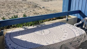 En balkong med ett bord och stolar, med utsikt över en strand med sand och gles vegetation.