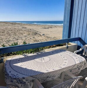 A balcony with a table and chairs, overlooking a beach with sand and sparse vegetation. - Ocean view (50m), dune, forest, comfortable studio. Tranquil beauty. (Mimizan plage)