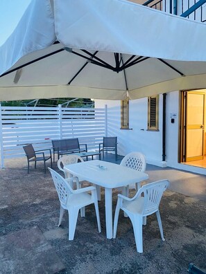 An outdoor patio with a white table and chairs, a large umbrella, and a white fence.