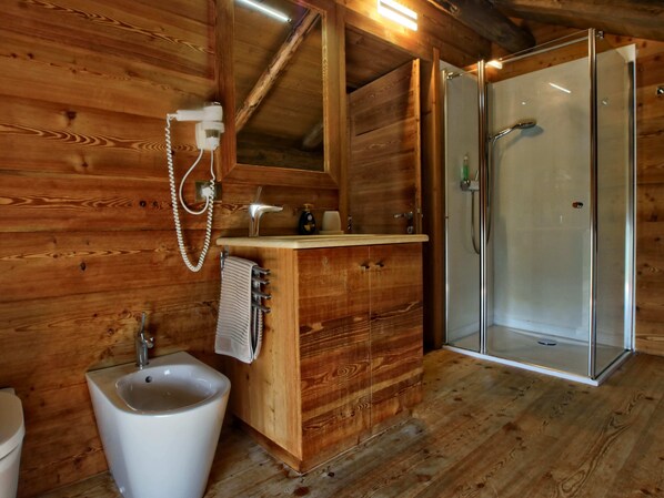 Une salle de bain rustique, aménagée dans une cabane en bois, avec un lavabo, un miroir, un porte-serviettes et une douche à parois de verre.