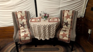 Ein gemütliches Zimmer mit karierter Tischdecke, zwei Stühlen mit Sternenmuster-Quilts, einem kleinen Tisch mit Blumenvase und Holzboden.