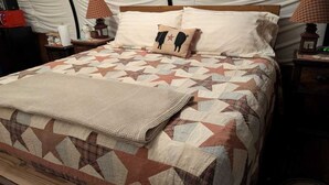 Ein Bett mit einer gesteppten Decke mit geometrischen Mustern, einem Kissen mit Schweinedruck und einer Nachttischlampe.