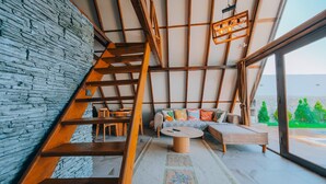 Un interior moderno con una escalera de madera, una pared de piedra, un sofá con cojines de colores y vistas amplias a través de grandes ventanales.
