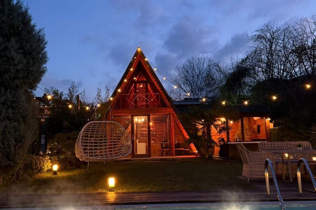 Una cabaña acogedora con piscina, rodeada de luces cálidas y una entrada bien iluminada.