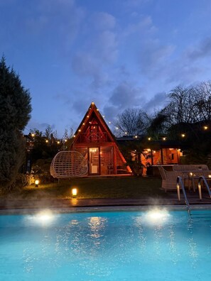 Una cabaña acogedora con piscina, rodeada de luces cálidas y una entrada bien iluminada.