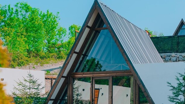 Una casa moderna con techo triangular, piscina y abundante vegetación.