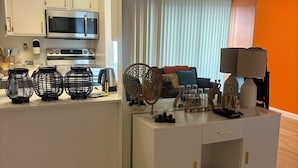 Ein modernes Wohnzimmer mit einem weißen Unterhaltungsschrank, einer Küchenzeile mit Geräten und einem großen Spiegel, der den Raum reflektiert.