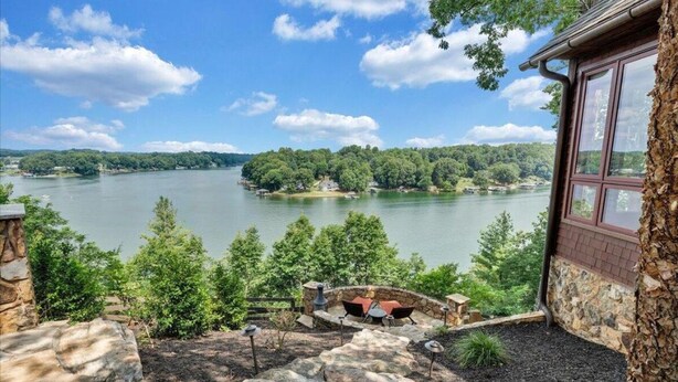 Una propiedad frente al lago con un patio de piedra, mobiliario exterior y vistas al lago y colinas boscosas.
