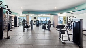 Un gimnasio amplio con diferentes máquinas de ejercicio, ventanas grandes y un techo curvo.