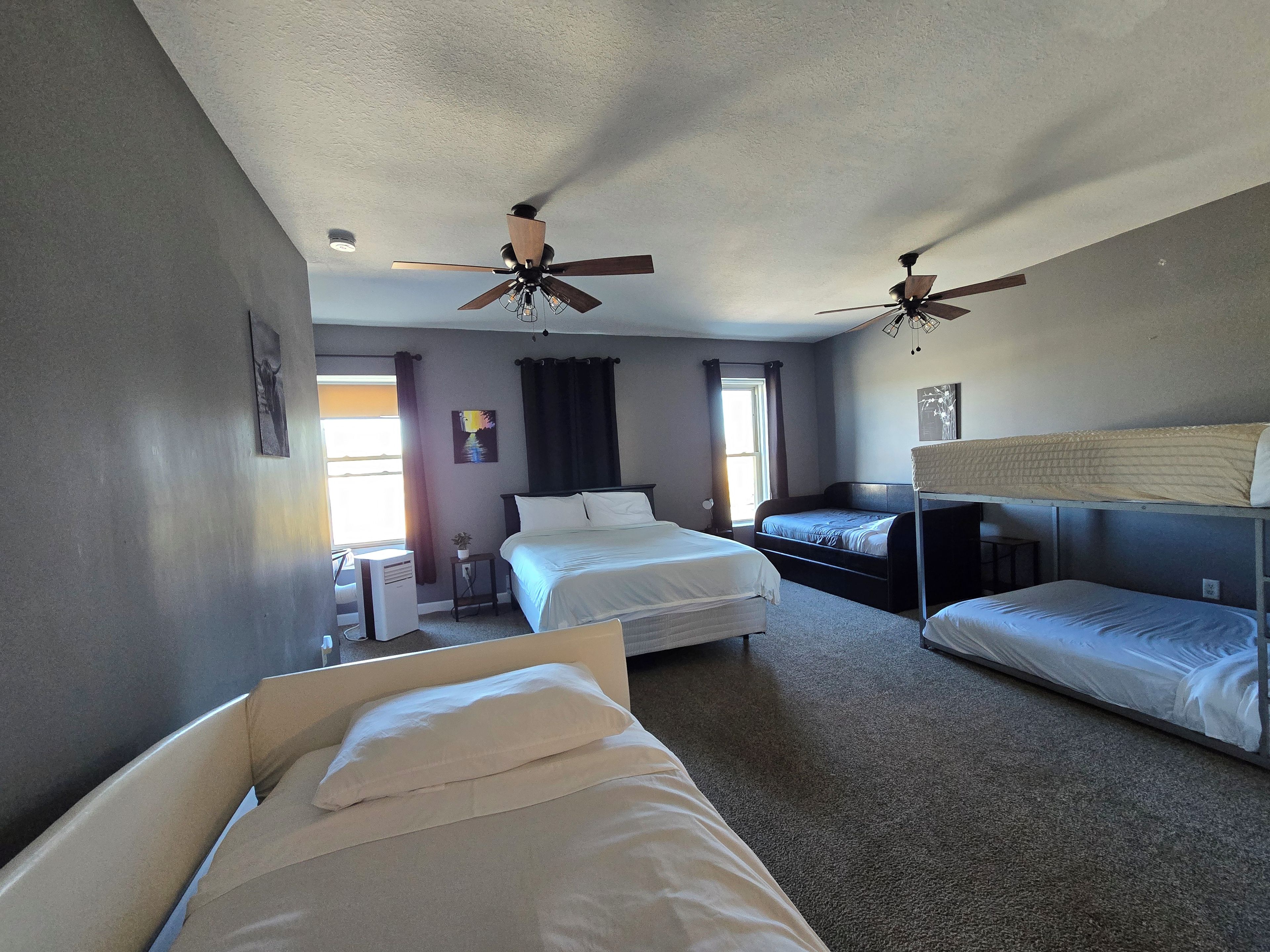 A hotel room with two beds, a ceiling fan, a window with curtains, and a small table with a plant.