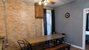 Un comedor con pared de ladrillo, mesa de madera, sillas de metal y un banco.