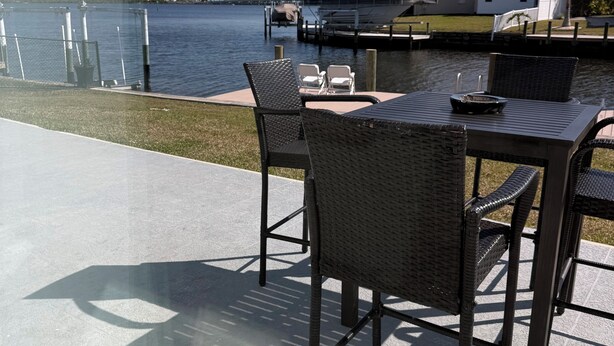 A patio with a table and chairs overlooking a body of water, a dock, and a house in the background. - Port Charlotte 3-2 waterfront home with dock and river view (Port Charlotte)