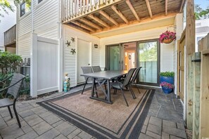 Eine Terrasse mit Tisch und Stühlen, eine Holzbeschichtung und eine Glastür zum überdachten Bereich.