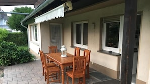 A patio with a wooden table and chairs, a lantern, and a covered area with windows.