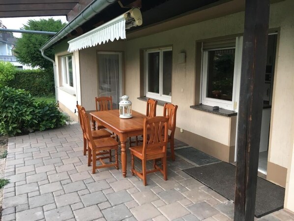 A patio with a wooden table and chairs, a lantern, and a covered area with windows. - Large apartment for fitters in Troisdorf | 100 sqm | up to 5 pers. | garden | parking lot (Troisdorf)