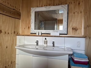 A bathroom with wooden walls, a white sink with two faucets, a mirror above the sink, and a stack of towels. - Large apartment for fitters in Troisdorf | 100 sqm | up to 5 pers. | garden | parking lot (Troisdorf)