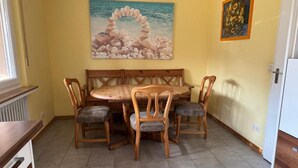 A dining area with a wooden table and chairs, a painting of a stone arch over water, and a framed picture on the wall.