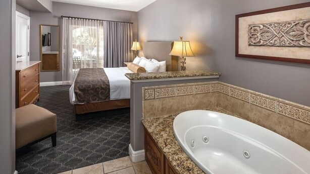 Ein Hotelzimmer mit Bett, einer Sitzecke mit Sessel, einer großen Badewanne und einem Fenster mit Vorhängen.