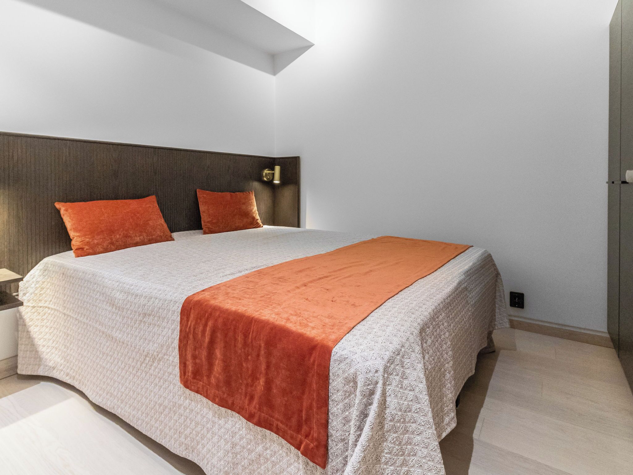 A modern bedroom with a large bed, two pillows, a nightstand, and a wardrobe.