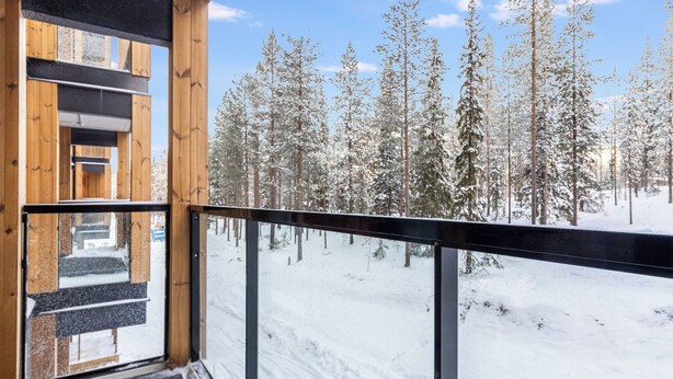 Un bâtiment en bois doté d’un balcon donnant sur une forêt enneigée.