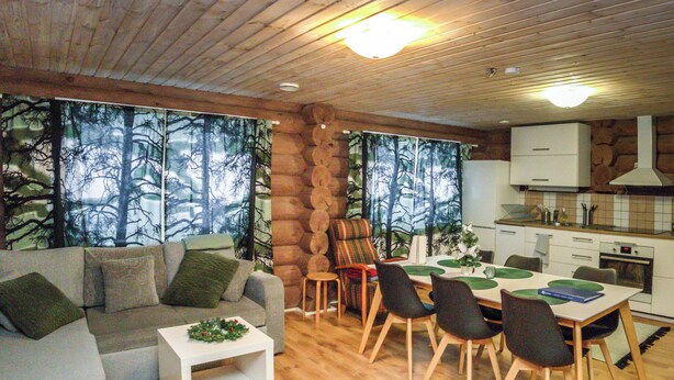 Un salón acogedor con sofá, mesa de centro y un comedor con sillas y una mesa. Se ve una cocina con estufa y armarios al fondo.