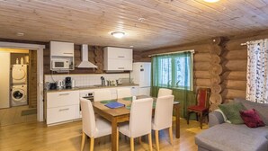 L’intérieur chaleureux d’un chalet avec un plafond en bois, un coin repas comprenant une table et des chaises, une cuisine équipée et un salon avec un canapé.