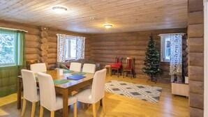 L’intérieur d’un chalet confortable, avec une salle à manger, deux fenêtres ornées de rideaux, un sapin de Noël et une cheminée.