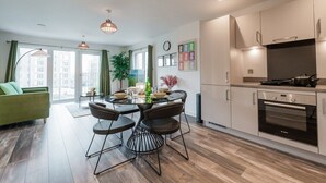 A modern kitchen with a built-in oven, a dining area with a round table and chairs, and a green sofa in a living room with large windows. - City Central | Free Parking | O2 | University (Birmingham)