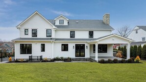Une maison à deux étages avec un porche à l’avant, une cheminée et une pelouse bien entretenue.