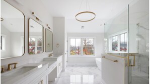 Une salle de bain moderne avec un sol en marbre blanc, une grande fenêtre offrant une belle vue et des accessoires dorés.