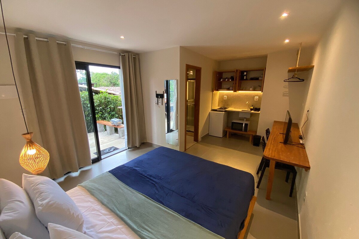A bedroom with a large bed, a small kitchenette, and a sliding glass door leading to a balcony.