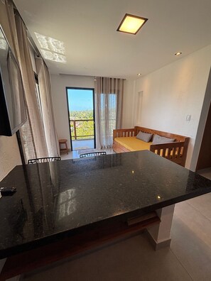 A modern room with a black marble countertop, a wooden bed with pillows, a large window with curtains, and a balcony with a view. - Villa Visgo Itacaré (Itacaré)