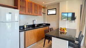 A modern kitchen with a refrigerator, sink, and wooden paneling, a dining area with a table and chairs, and a TV mounted on the wall. - Villa Visgo Itacaré (Itacaré)