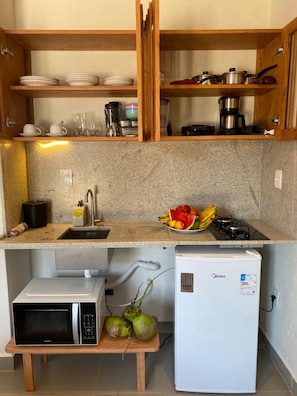 A compact kitchen with a microwave, refrigerator, and a small table with coconuts. - Villa Visgo Itacaré (Itacaré)