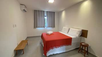 Une chambre d’hôtel avec un lit, un banc, une fenêtre avec des rideaux et un luminaire au plafond.